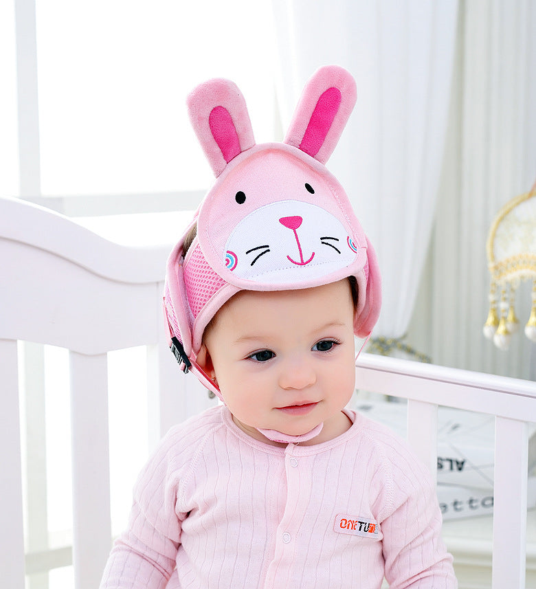 A baby wearing a pink knit onesie and a cute pink helmet with bunny ears sits in a white crib. Soft lighting and pastel colors create a cozy and playful atmosphere.