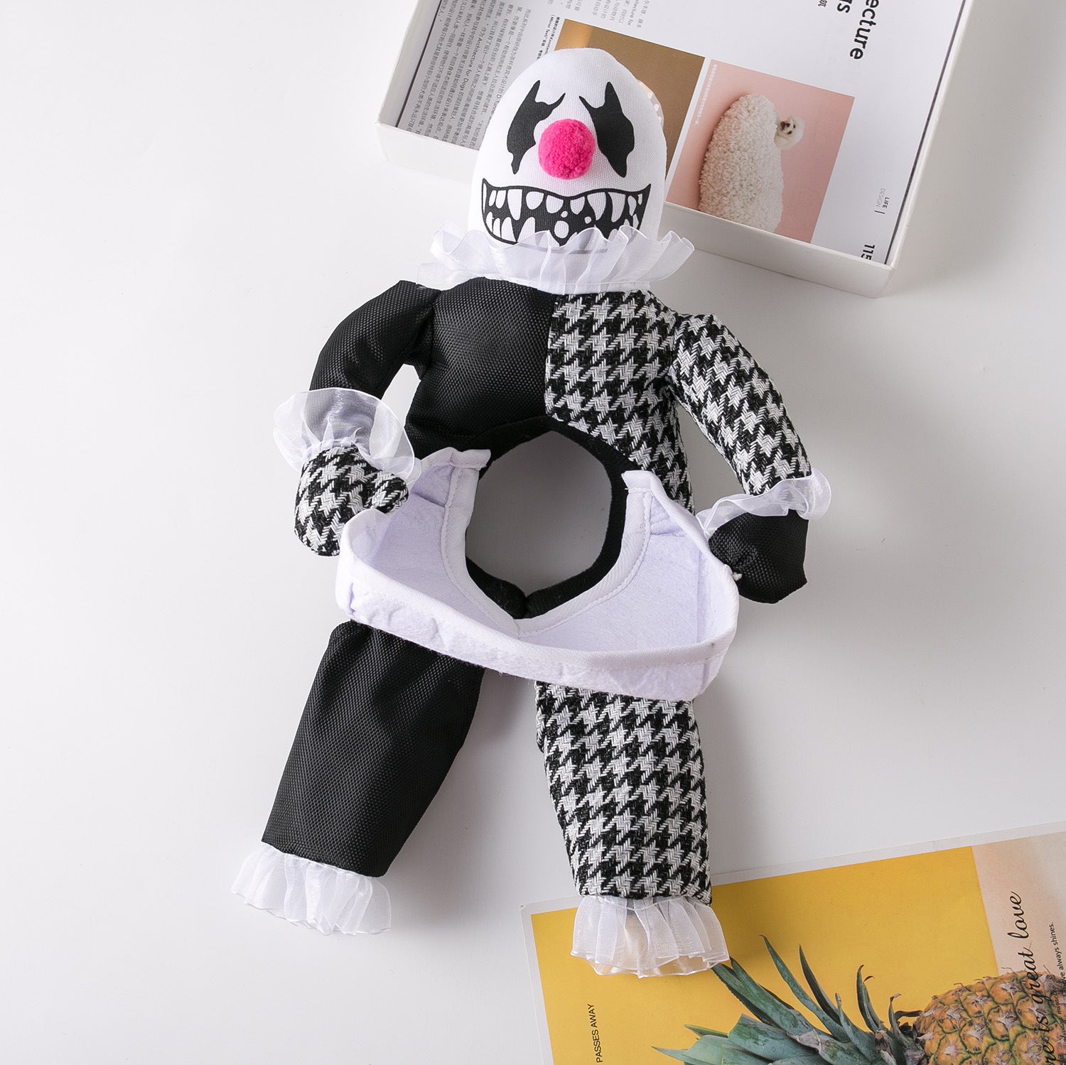 Plush clown costume for pets, featuring black and white houndstooth pattern. It has a frilly white collar, pink nose, and tribal-style makeup design, displayed on a white surface.