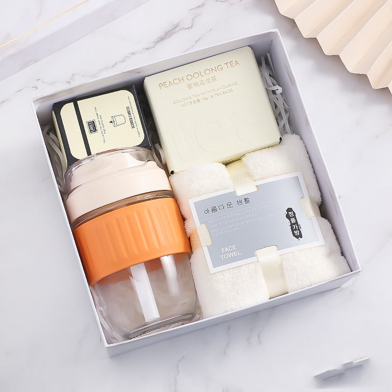 Gift box containing peach oolong tea, a small container, a tumbler with orange grip, and a white face towel, set against a marble background.