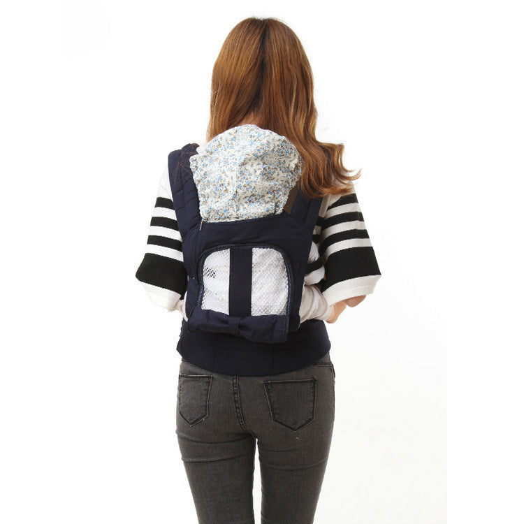 Woman with long hair wearing a black and white striped sweater and gray jeans, seen from the back. She carries a baby in a navy blue floral-patterned carrier.