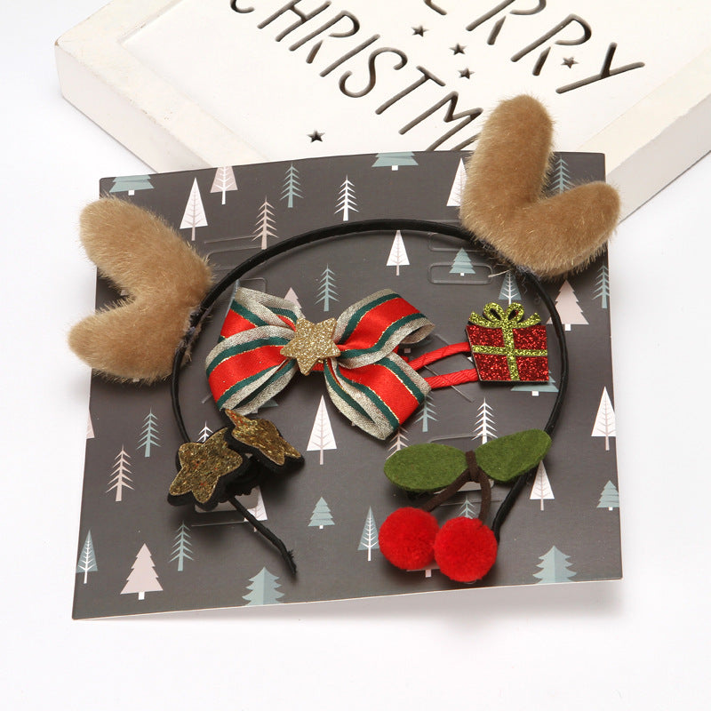 Festive headband with fluffy antlers, striped bow, red gift, cherries, and star embellishments on Christmas-themed background featuring small trees.