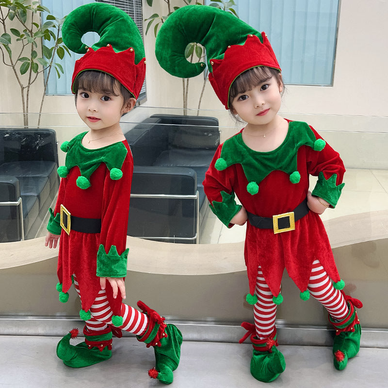 Two young children in matching red and green elf costumes with striped leggings and pointy hats, posing indoors with a festive, cheerful expression.
