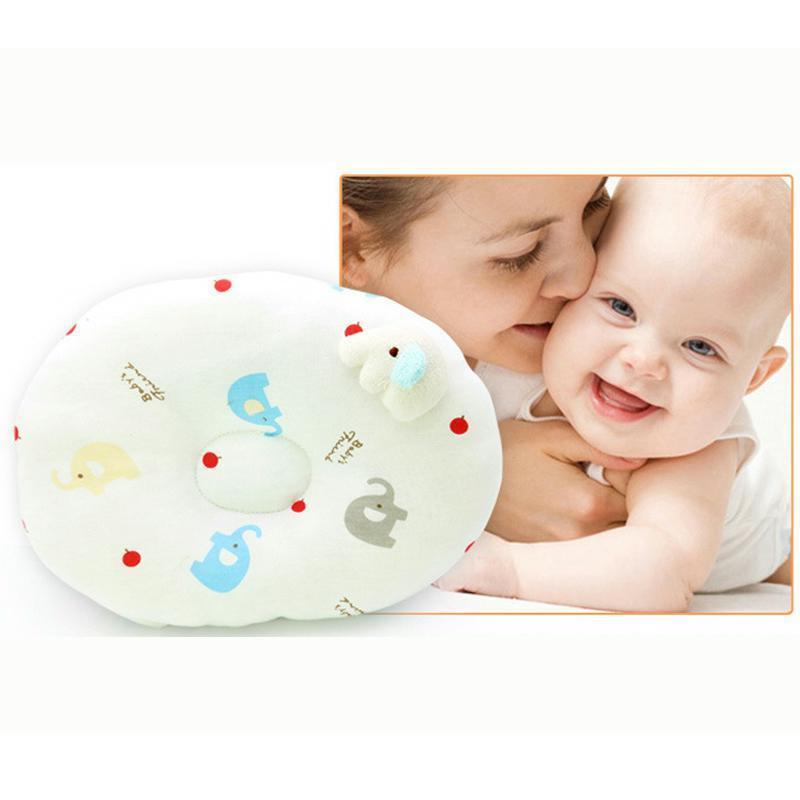 A smiling baby is lovingly embraced by a woman in the background. In the foreground, there is a cute baby pillow with colorful elephant and apple prints.