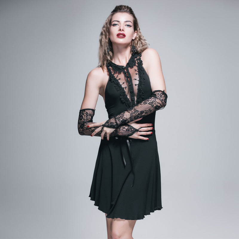 Woman in a black lace dress poses confidently against a gray background, with lace arm warmers and red lipstick adding to the elegant, dramatic look.