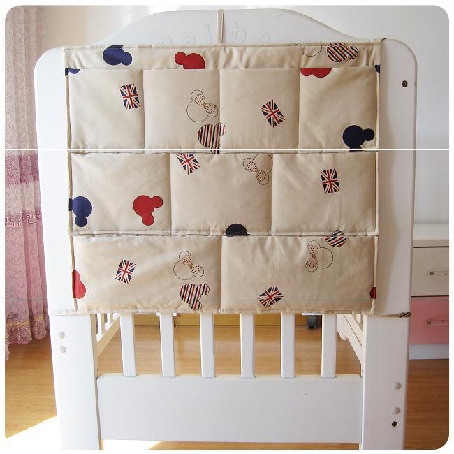 Beige crib rail cover with playful prints of red and blue mouse silhouettes, British flags, and striped patterns, attached to a white crib.