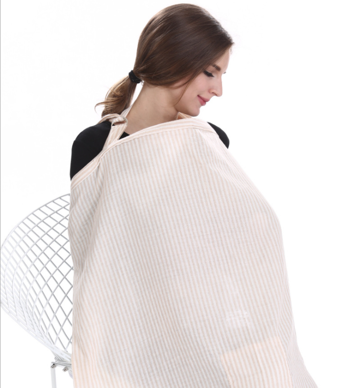 A woman with dark hair is seated in a white wire chair, wearing a beige striped nursing cover draped from her neck, with a gentle and content expression.