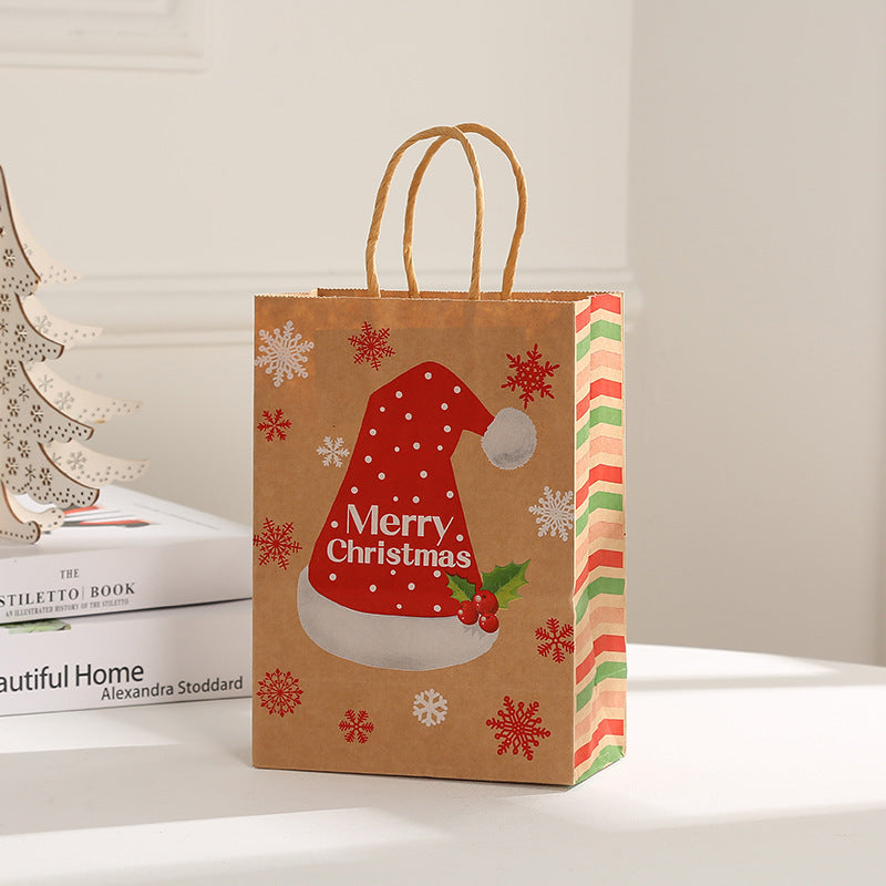 Festive brown paper bag with "Merry Christmas" on a red Santa hat, snowflakes, holly, and zigzag stripes. It's set in a cozy room with a white book and wooden tree decoration.