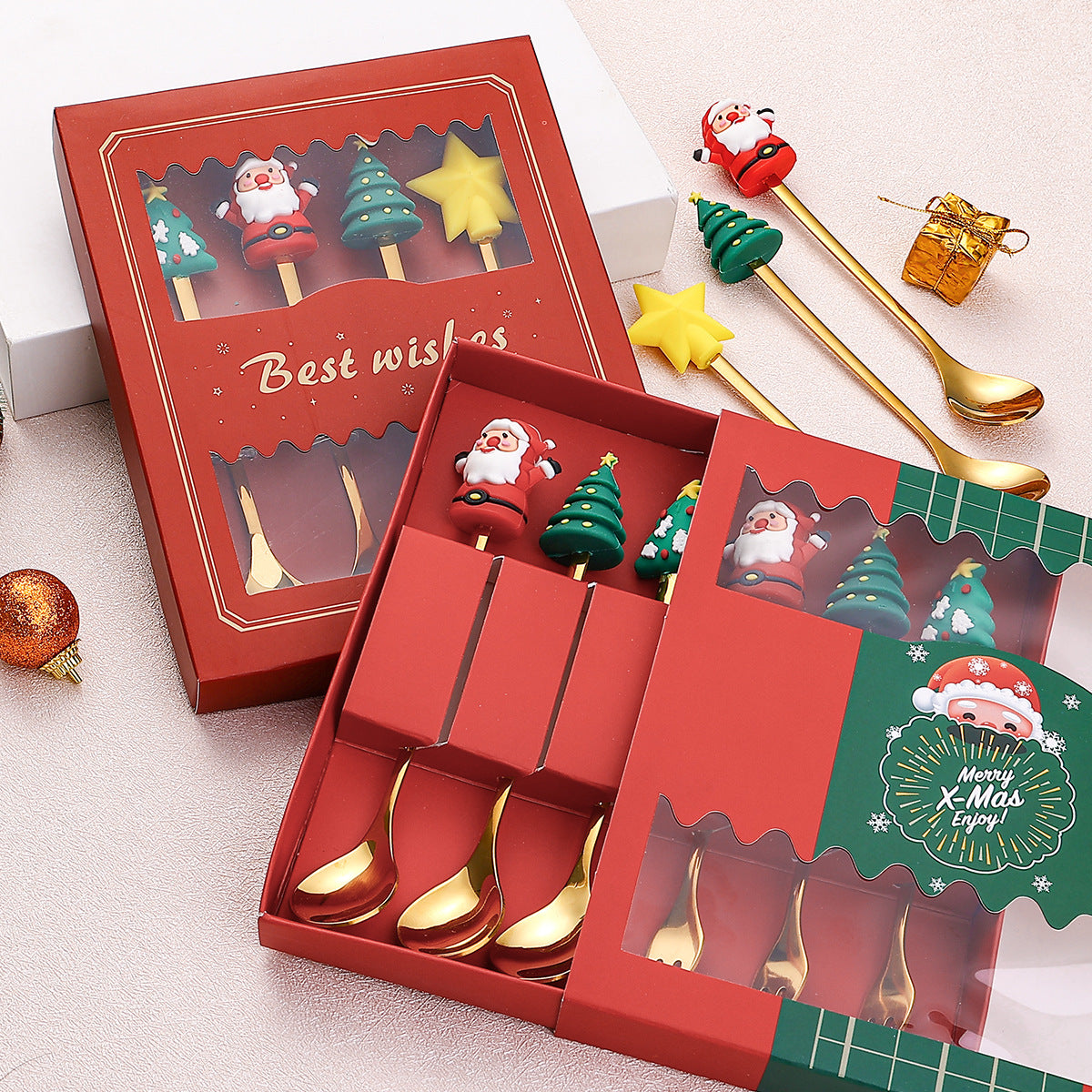 Red gift boxes containing gold spoons with festive handles featuring Santa, Christmas trees, and stars. Decorative elements like ornaments and a small gold gift are nearby.
