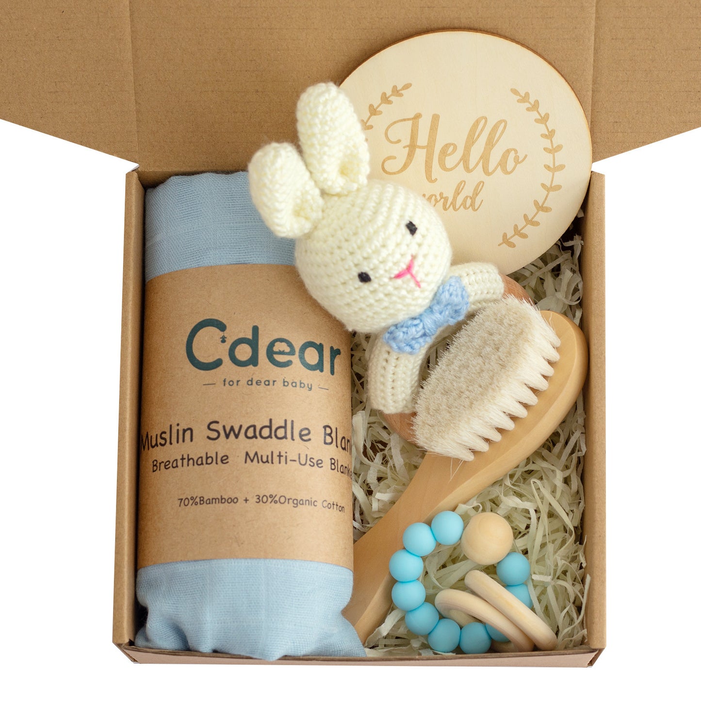 Gift box with a blue muslin swaddle, crochet bunny rattle, wooden hairbrush, and a "Hello World" wooden disc, surrounded by shredded packing material.