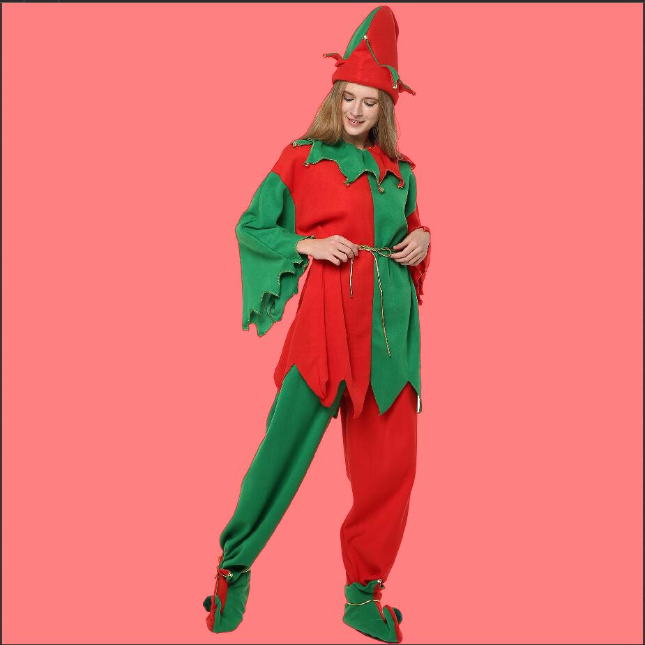 A person in a festive red and green elf costume with a pointed hat and curled shoes poses against a solid pink background.