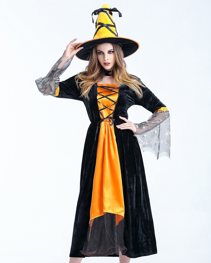 Woman in a black and orange witch costume with lace sleeves, wearing a matching pointed hat, posing with one hand adjusting the brim, against a plain backdrop.