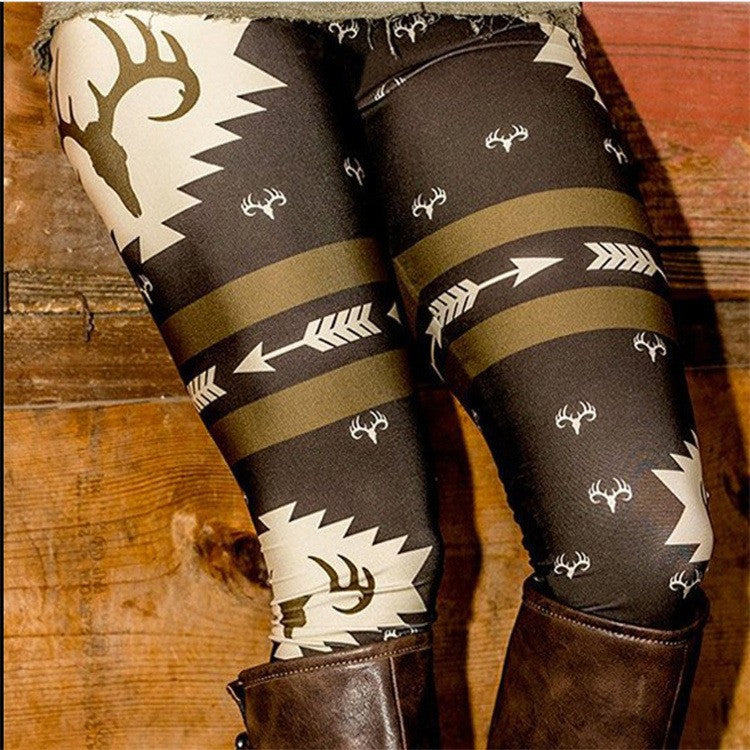 Brown leggings with bold tribal patterns, featuring deer antlers and arrows, paired with dark brown leather boots. The background is a rustic wooden surface.