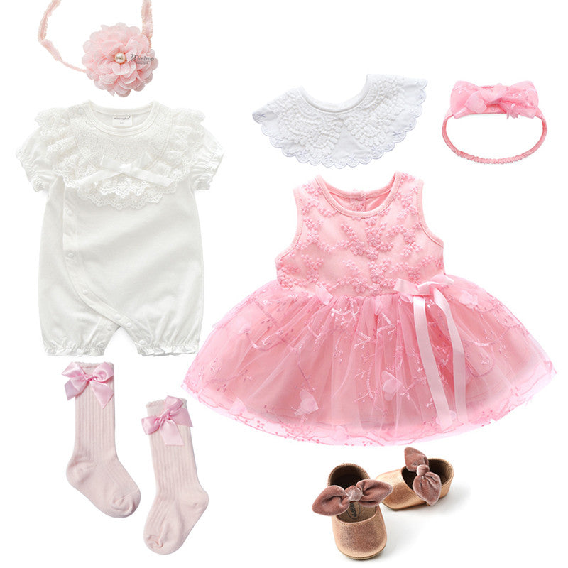 A baby clothing set featuring a pink embroidered dress, white romper, two headbands, a detachable collar, pink socks with bows, and brown shoes with bows.