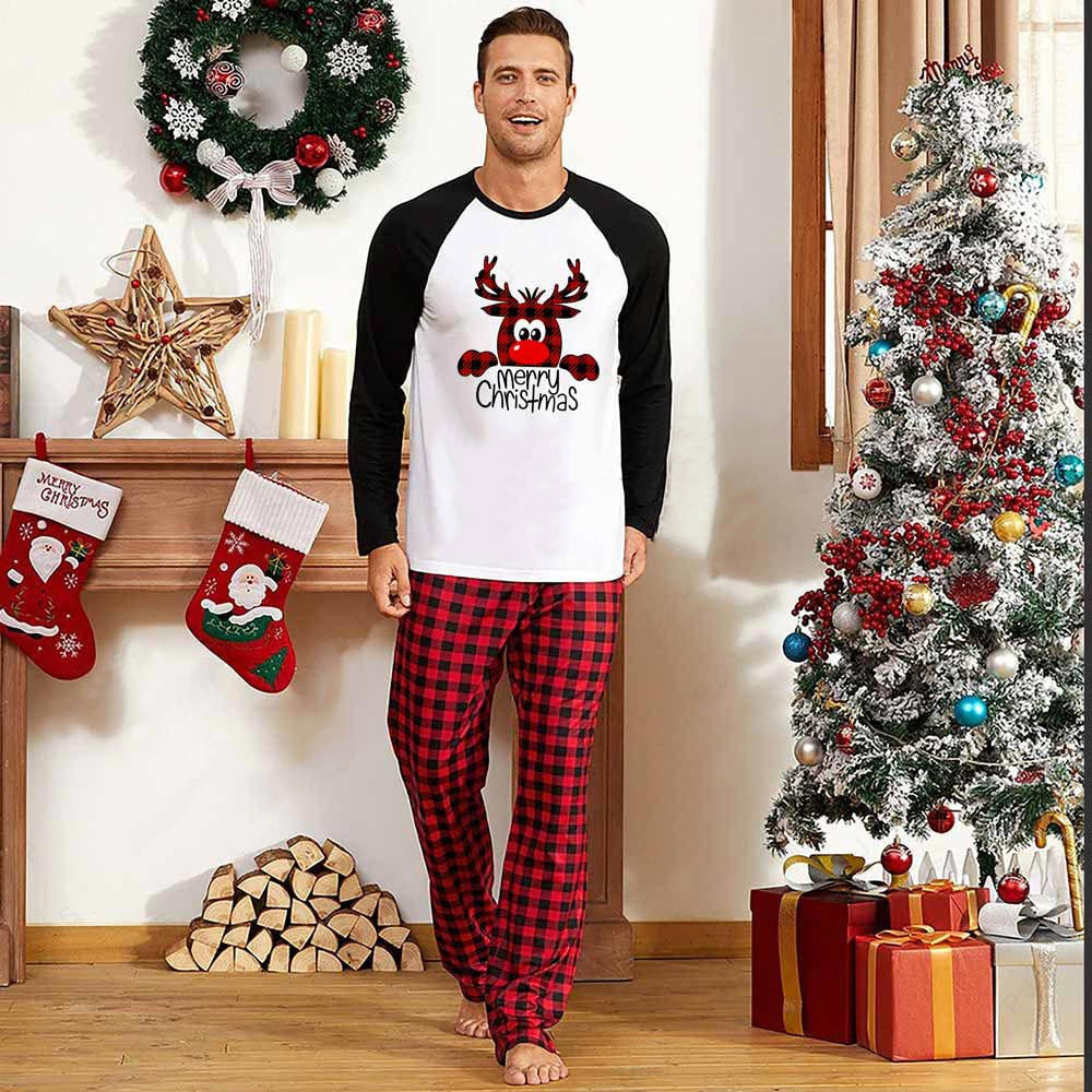 A person in festive pajamas stands by a Christmas tree. The fireplace is adorned with stockings and a wreath. A pile of presents sits under the tree, enhancing the holiday spirit.