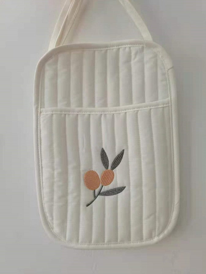 White quilted fabric bag with a simple design featuring two embroidered oranges and green leaves. The bag has two handles and vertical stitching, giving it a textured appearance.