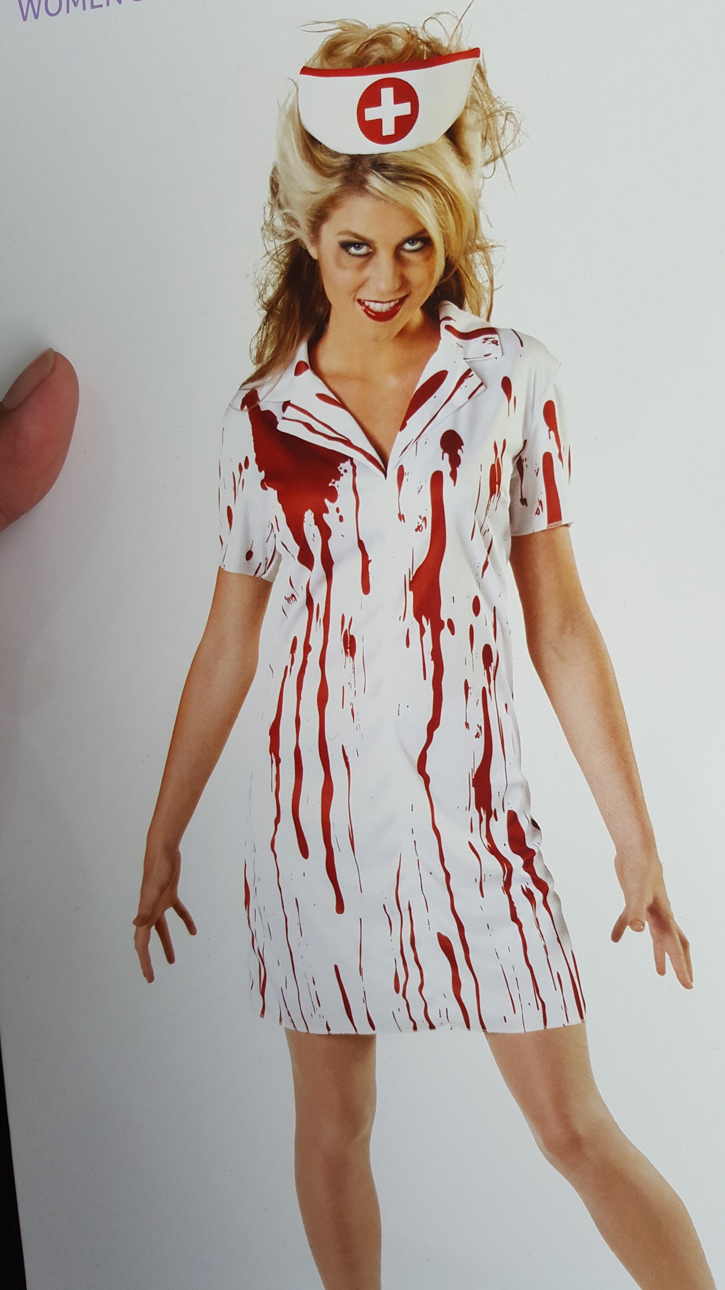 Person in a white nurse costume stained with red, wearing a nurse hat, has disheveled hair and a playful expression, standing against a plain background.