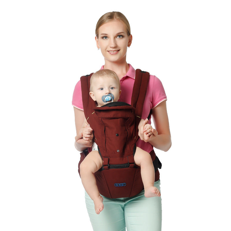 A woman in a pink shirt smiles while carrying a baby with a pacifier in a maroon baby carrier, standing against a white background.