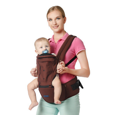 A woman in a pink polo shirt smiles while carrying a baby in a brown front-facing baby carrier. The baby, wearing a blue pacifier, looks content.