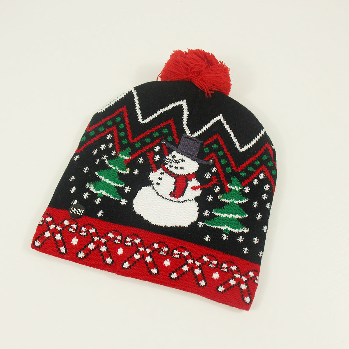 A festive black knit hat featuring a snowman, green trees, and snowflakes. The red brim is adorned with candy cane patterns, topped with a red pom-pom.