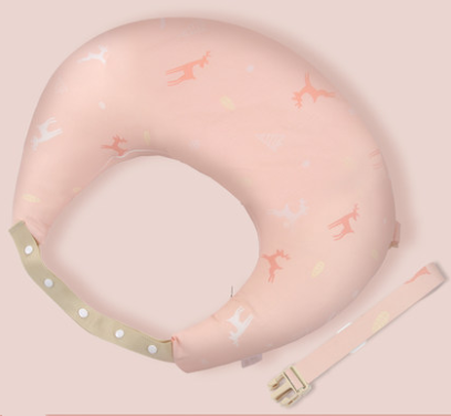 A pink crescent-shaped nursing pillow with a playful animal pattern, featuring antlers. It includes a detachable beige strap with snap fasteners and a buckle, displayed on a matching pink background.