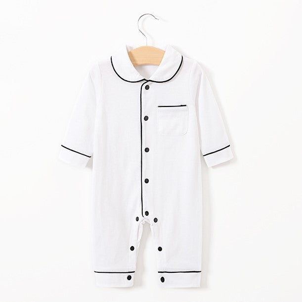 White baby romper with black trim on the collar, cuffs, and button line. It features a front pocket and black buttons. Hanging on a wooden hanger against a white background.