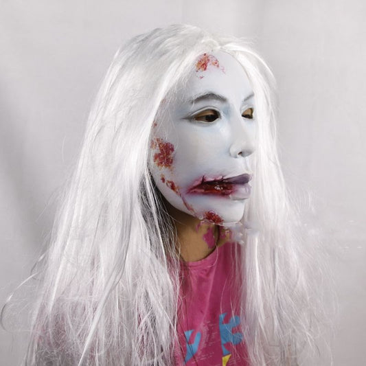 A person wearing a white, long-haired wig and a white mask with red marks, dressed in a pink shirt. The background is plain white, creating a stark contrast.