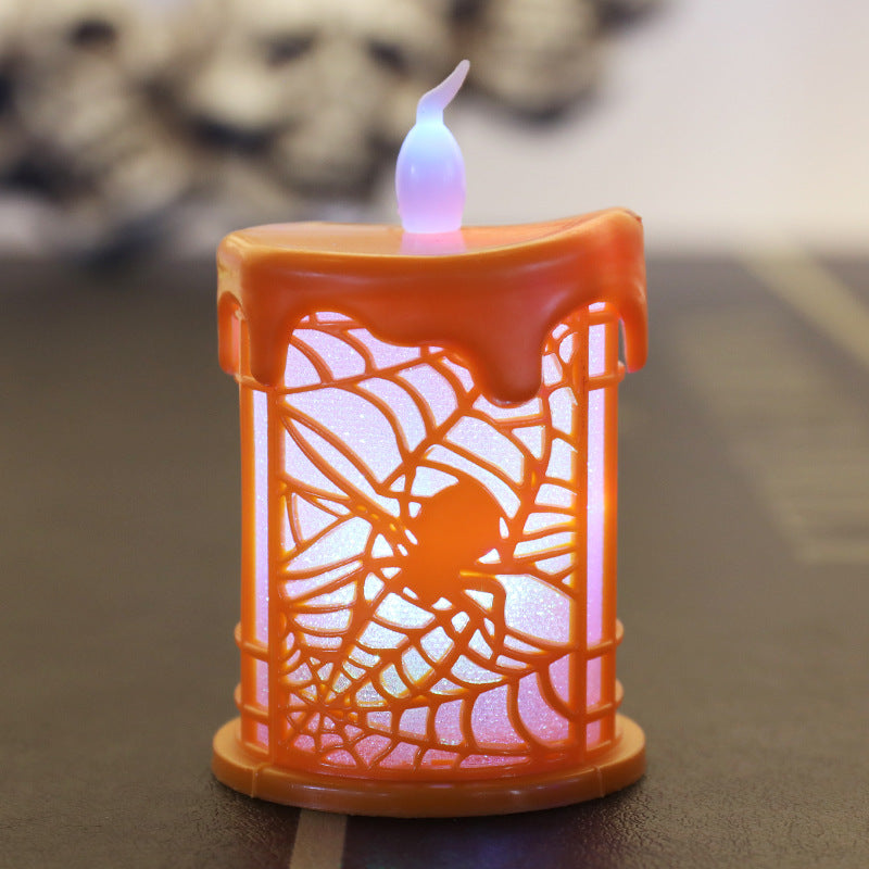 An orange candle with a melting wax design features a carved spider and web pattern. The candle emits a soft glow, illuminating the intricate web details. It stands on a flat surface with an unfocused background, enhancing its decorative and spooky appearance.