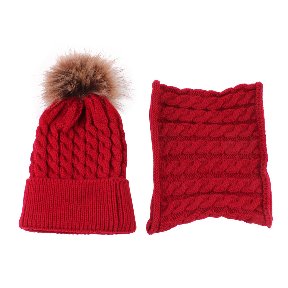Red knit winter set with a beanie and matching scarf. The hat features a faux fur pom-pom and cable knit pattern. The scarf has a similar cable design.