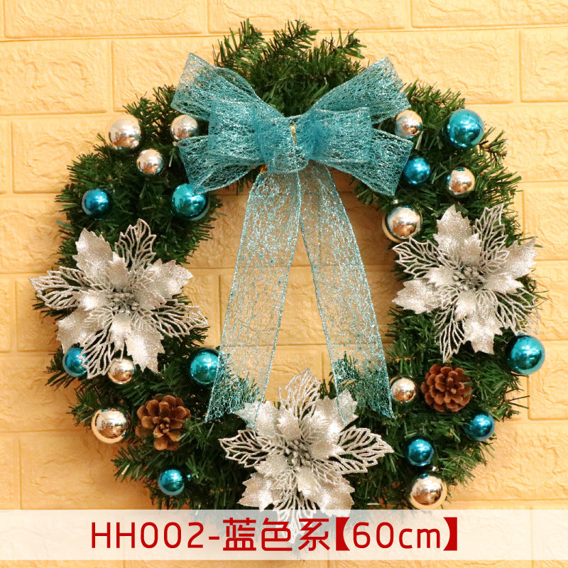 Festive wreath with teal ribbon, silver poinsettias, and blue and silver ornaments on a green base. Decorative pine cones are scattered throughout. Size noted as 60cm.