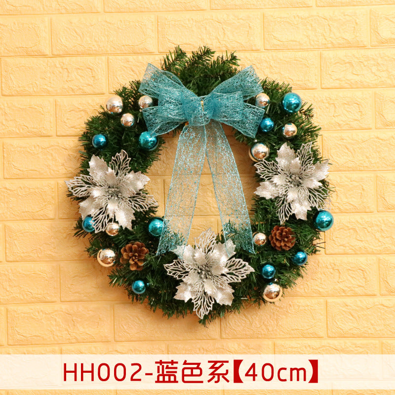 Festive wreath with silver poinsettias, blue and silver ornaments, pinecones, and a blue ribbon, set against a yellow brick wall.