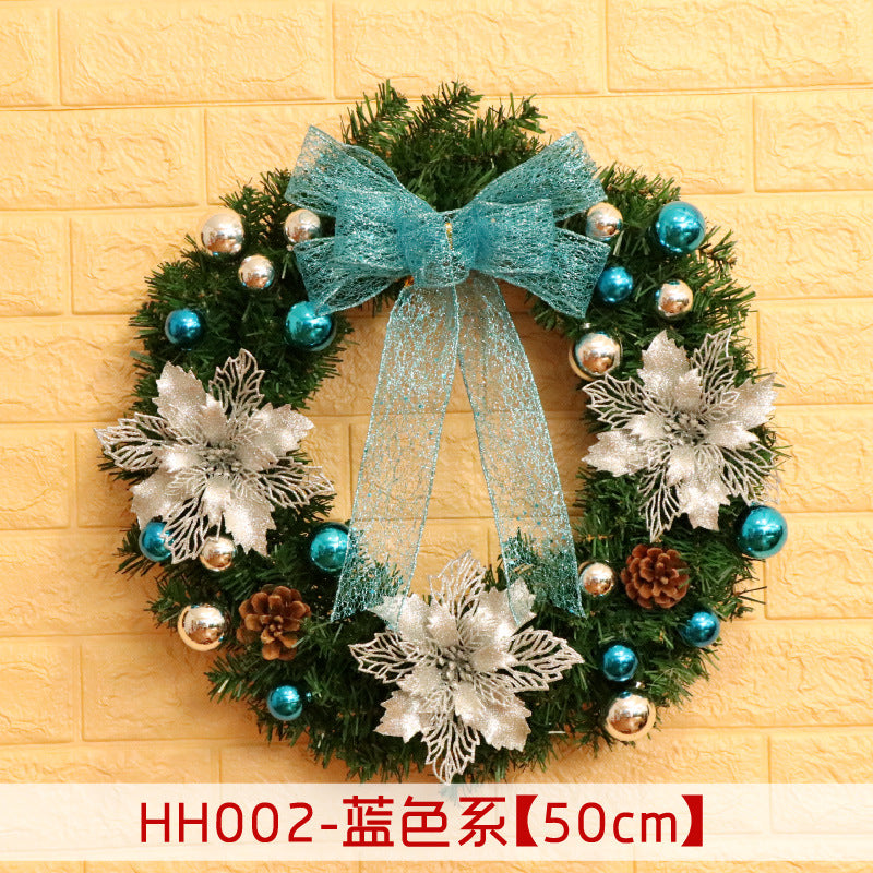 Festive wreath with teal bow, silver and teal ornaments, pinecones, and glittery silver poinsettias on a green base against a yellow brick background. Text reads "HH002-蓝色系【50cm】".