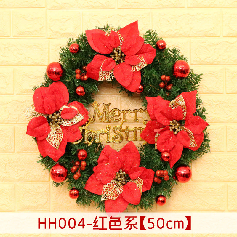 Festive Christmas wreath with red poinsettias, gold accents, and shiny red ornaments on a green base. The words "Merry Christmas" are in the center, displayed on a beige brick wall.