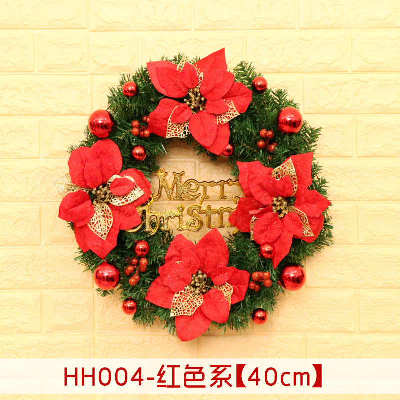 Christmas wreath with red poinsettias, gold accents, and red baubles on a green base, featuring a "Merry Christmas" sign in the center. Set against a light brick background.
