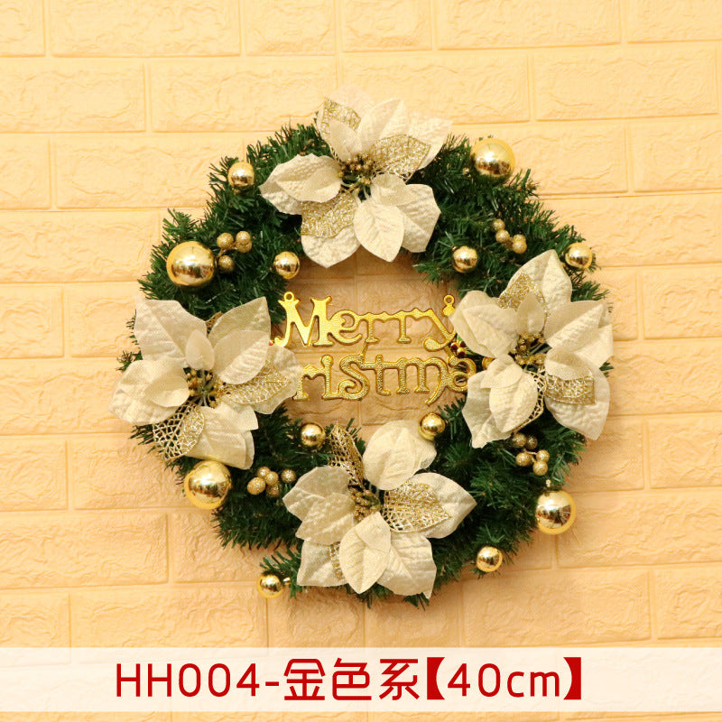 Christmas wreath with white flowers and gold accents on a brick wall. A "Merry Christmas" sign is in the center. The wreath has a mix of shiny gold balls and leaves.