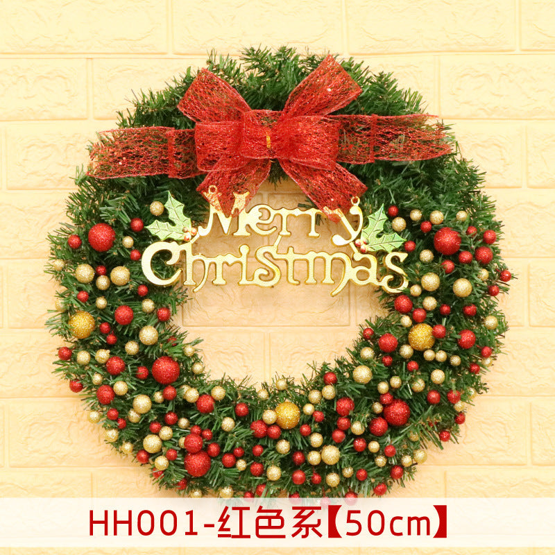 Festive Christmas wreath adorned with red and gold baubles, featuring a large red bow and "Merry Christmas" text, set against a light brick wall.