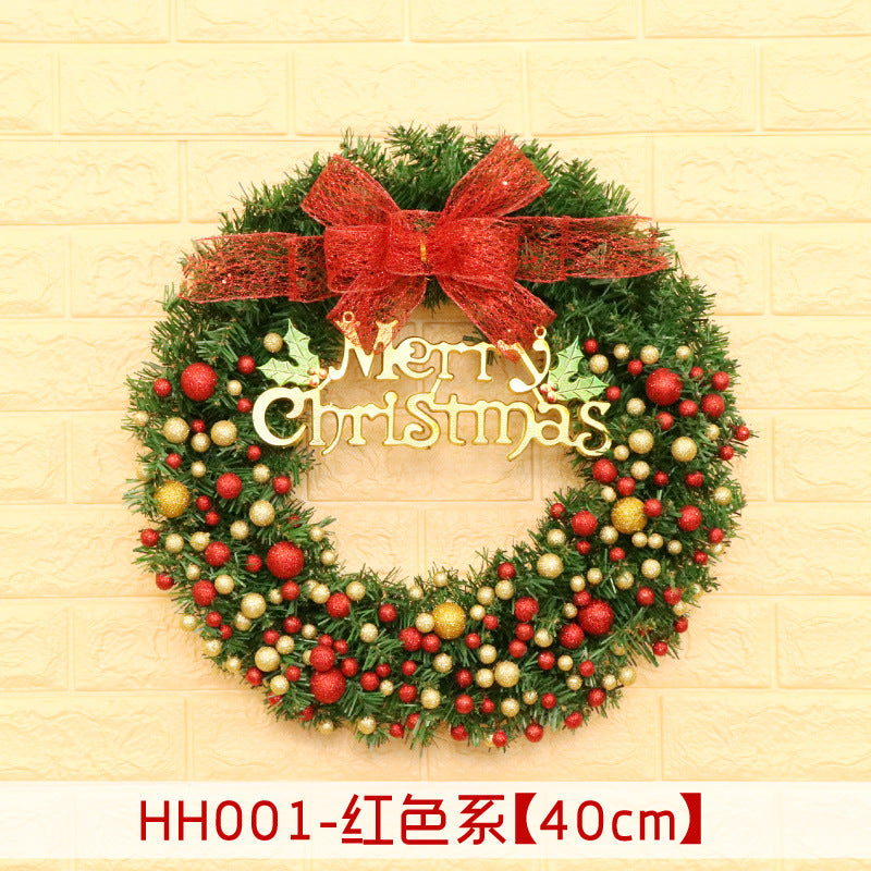 A Christmas wreath with red, gold, and green baubles, featuring a red bow and "Merry Christmas" text, is displayed against a light brick wall.