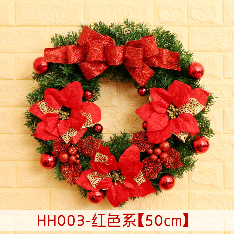 Festive wreath with red poinsettias, glittery leaves, shiny red ornaments, and a large bow, set against a light textured wall. 50cm diameter noted at the bottom.