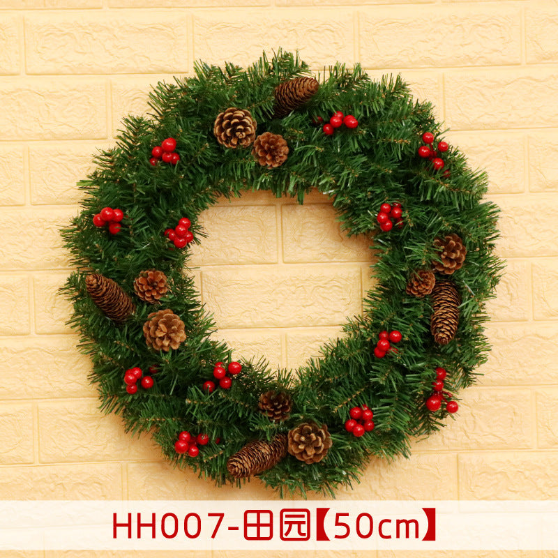 A festive wreath with green foliage, brown pinecones, and red berries, hanging on a textured yellow wall. The wreath measures 50 cm in diameter.