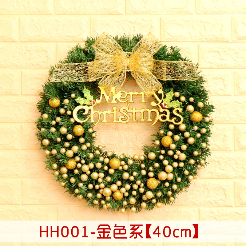 Festive Christmas wreath adorned with gold baubles and a sparkling bow, featuring "Merry Christmas" in golden text, set against a light brick wall.