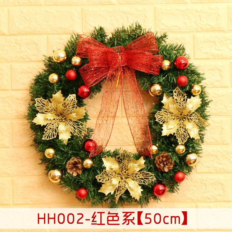 Festive Christmas wreath with gold flowers, red and gold ornaments, pinecones, and a large red bow, set against a light-colored brick wall.