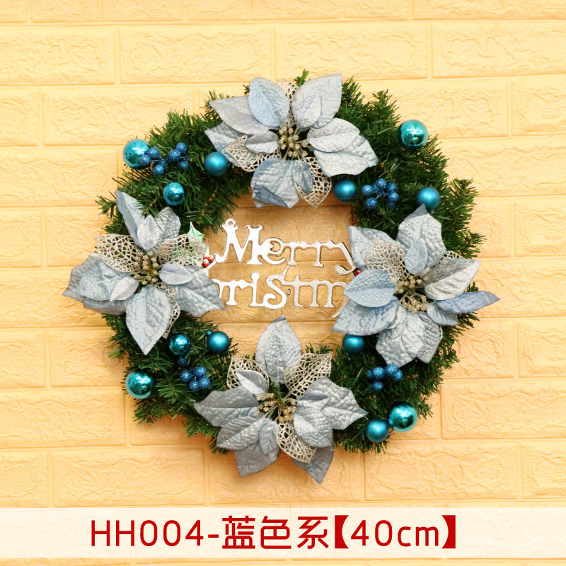 Christmas wreath with silver poinsettias and blue ornaments, featuring a "Merry Christmas" sign, hanging on a yellow brick wall.
