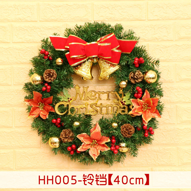 Christmas wreath with red bow, gold bells, poinsettias, pinecones, and baubles. "Merry Christmas" in gold lettering. Set against a light brick wall.