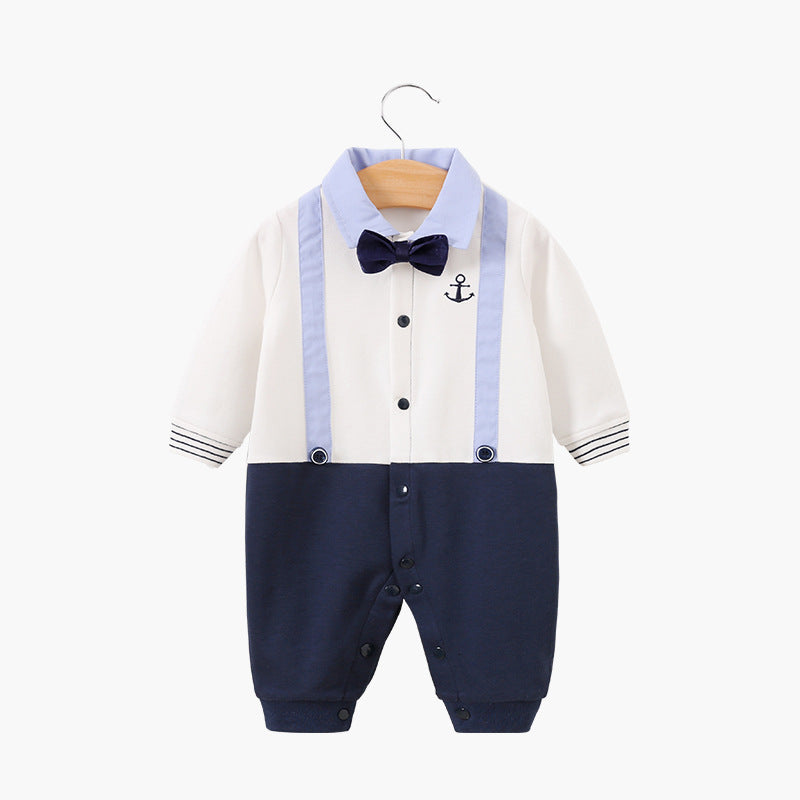Baby outfit on hanger, featuring white top with blue bow tie, anchor emblem, and blue suspenders. Navy bottom with snap buttons and striped sleeve details, for a nautical look.