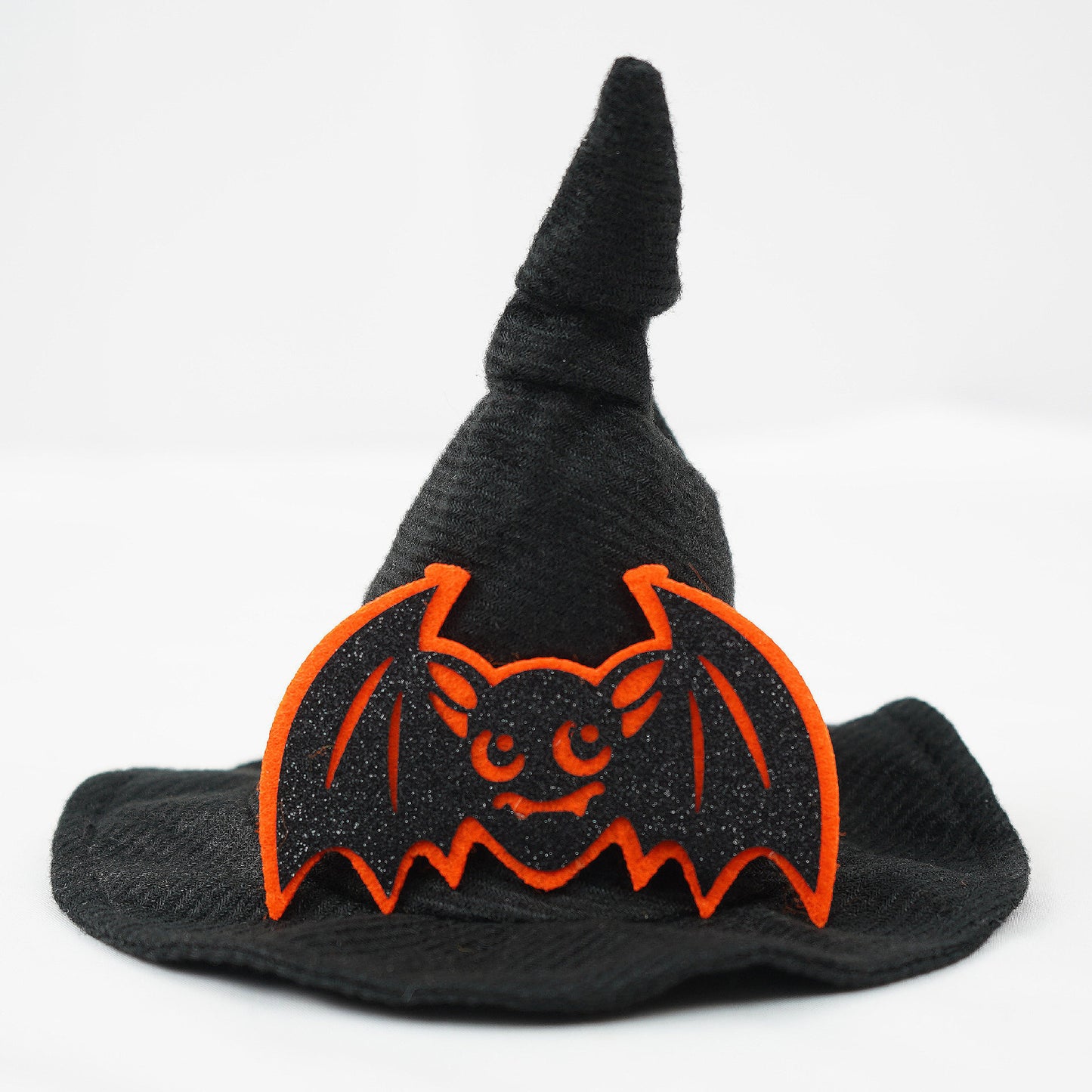 A black witch hat with a glittery bat decoration featuring bright orange outlines and a smiling face, set against a plain white background.