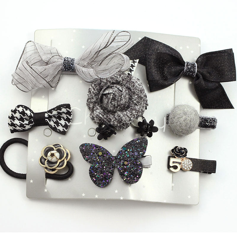 Set of black and gray hair accessories, including bows, a glittery butterfly, a fabric rose, a houndstooth bow, a felt ball, and a flower clip on a silver background.