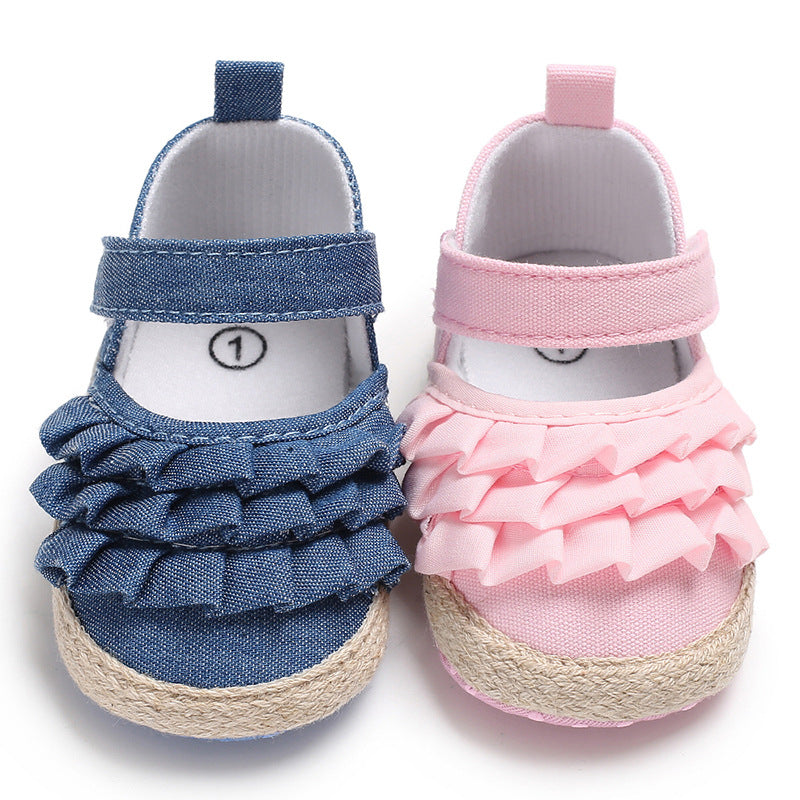 A pair of baby shoes with ruffled design: one blue shoe and one pink, both with Velcro straps and rope detailing at the sole, displayed side by side.