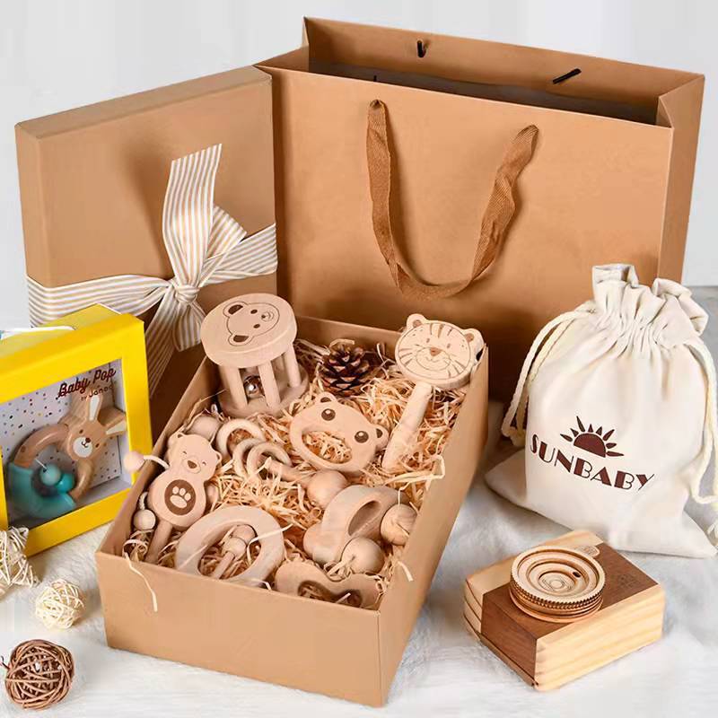 Gift set with wooden baby toys, including rattles and teethers, in a brown bag with a bow. A drawstring pouch and a yellow toy box are also visible.