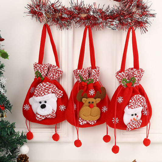 Three festive red gift bags with handles hang under tinsel. Each bag has holiday designs: a bear, a reindeer, and a snowman, all adorned with holly and snowflakes.