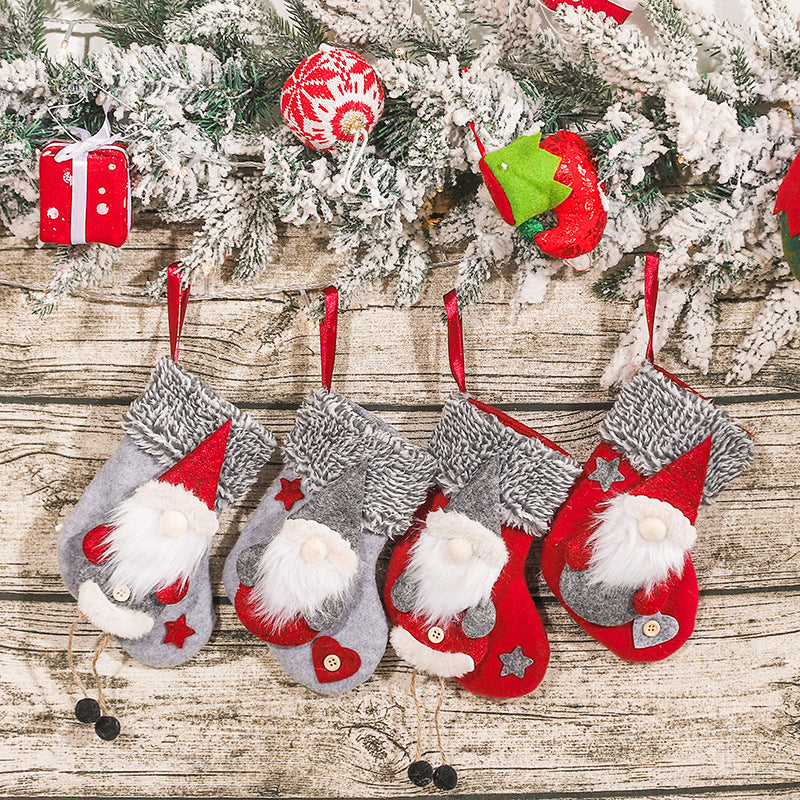 Four festive Christmas stockings featuring gnome designs hang on a wooden wall. Above them is a garland with snow-covered pine branches and colorful holiday decorations.