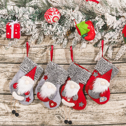 Four festive Christmas stockings featuring gnome designs hang on a wooden wall. Above them is a garland with snow-covered pine branches and colorful holiday decorations.